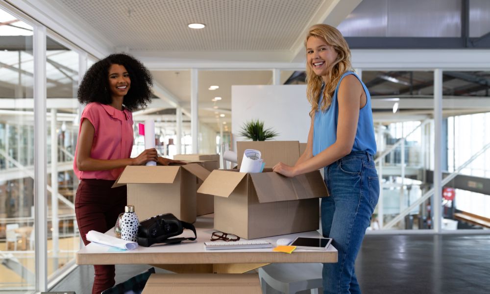 Portrait of young diverse female executives unpacking cardboard boxes in office. This is a casual creative start-up business office for a diverse team