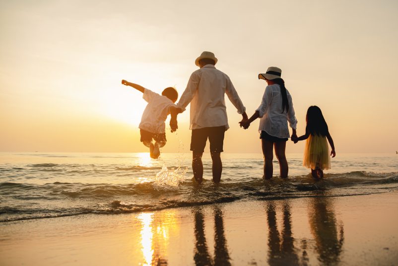 Happy asian family jumping together on the beach in holiday. Silhouette of the family holding hands enjoying the sunset on the  beach.Happy family travel and vacations concept.