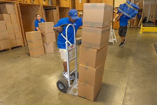 A man in a blue shirt and pants is moving boxes, featured in the Winter Storage Guide for San Marcos Facilities.