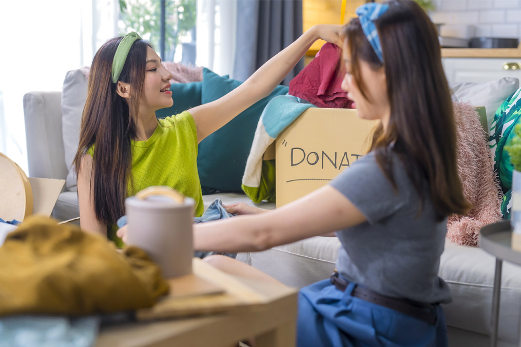 An Organizing clothes for donation, two women sorting items at home. They share smiles and laughter, creating positive atmosphere while decluttering Asian couple checking and sorting clothes donate